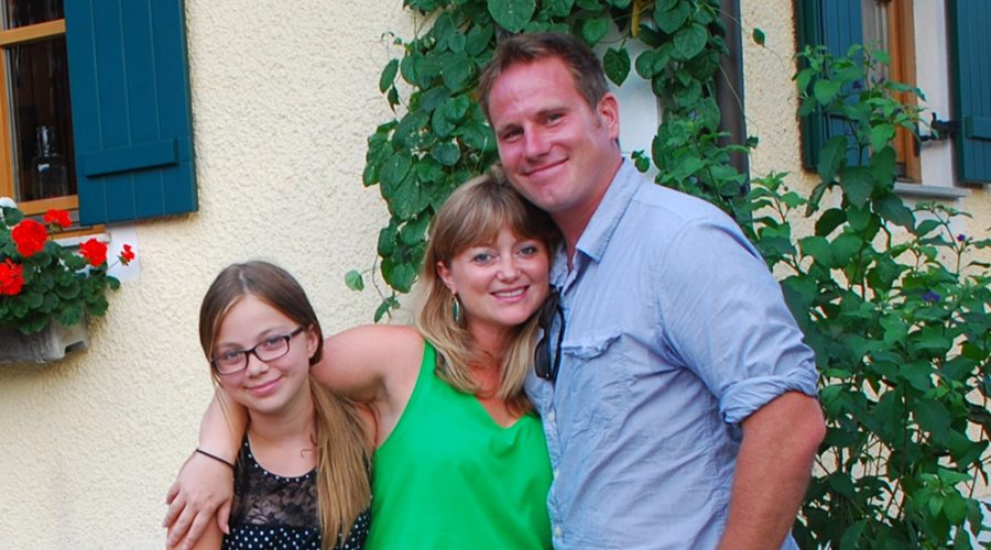 young girl with her parents standing in front of a house.