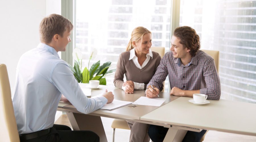 Young couple seated at a table with a Realtor, signing documents