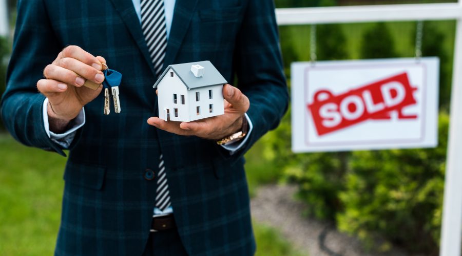 realtor holding keys and model house next to a sold sign